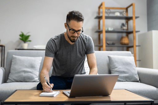 Professional creating content on a laptop while taking notes, representing focused thought leadership work in a modern workspace.